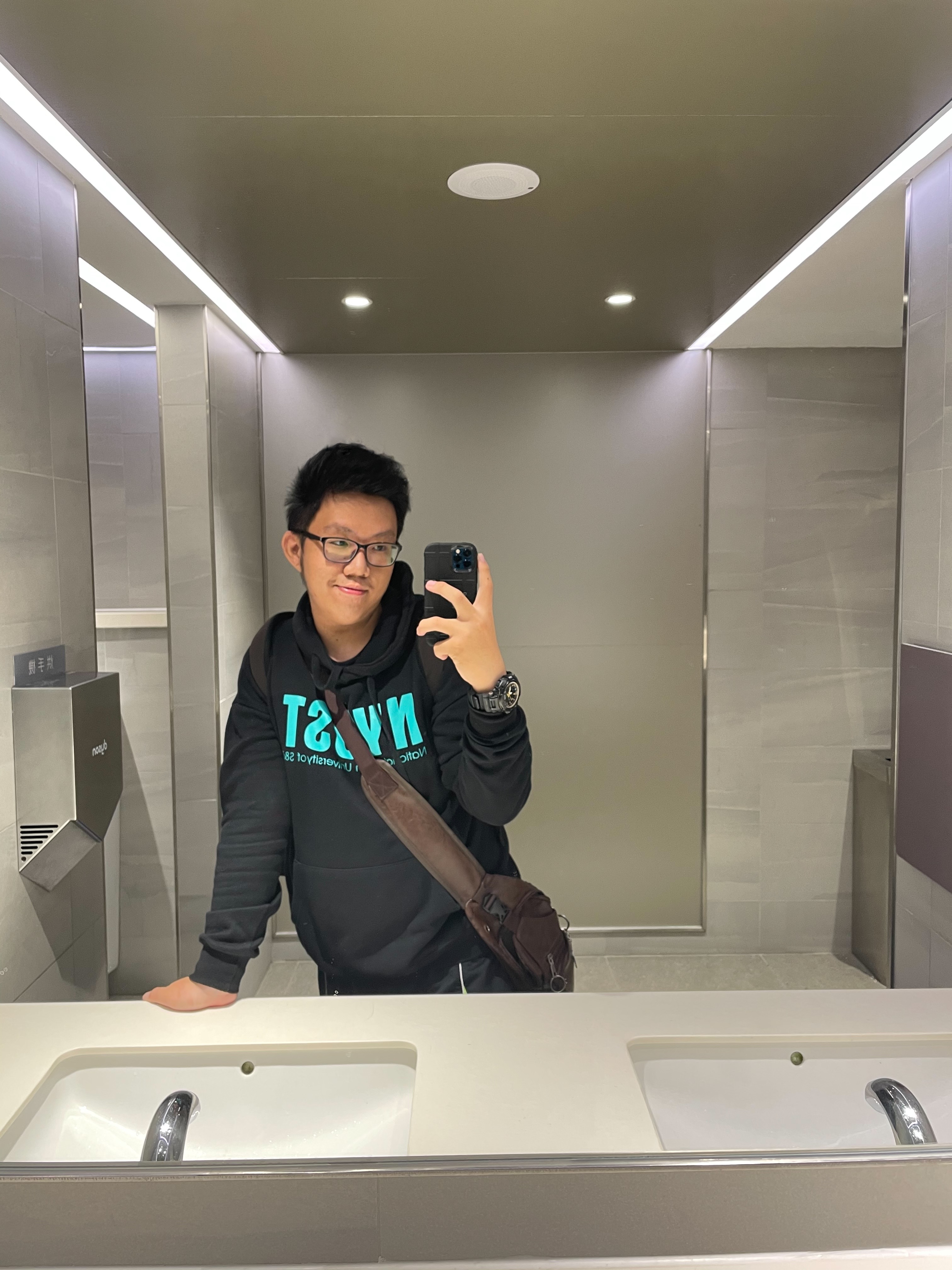 A Picture of me wearing a Black Yuntech Hoodie doing a mirror selfie in a restroom somewhere in Kaohsiung